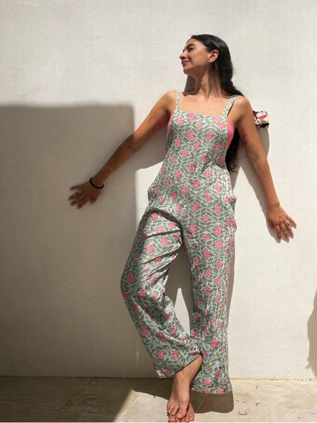 Woman wearing a floral jumpsuit standing against a white wall with sunlight casting shadows.