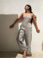 Woman wearing a floral jumpsuit standing against a white wall with sunlight casting shadows.